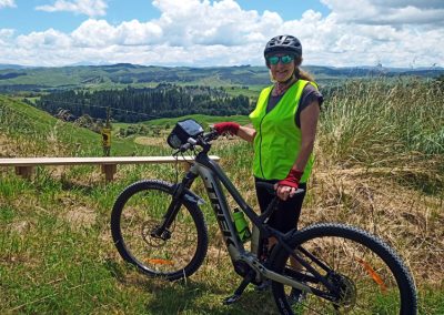 Adventure cyclist at the high point of the Laughing Moa Cycle trail, with high vis gear and green cloaked hills behind.